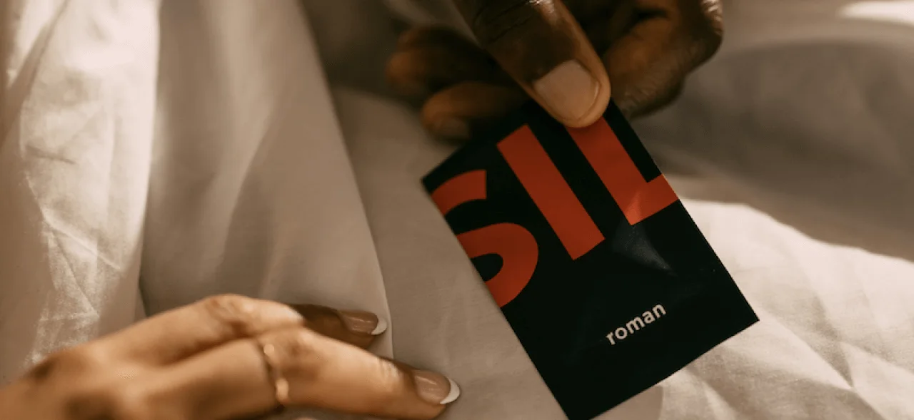 Man holding Sildenafil pills with Roman pill packet in bed